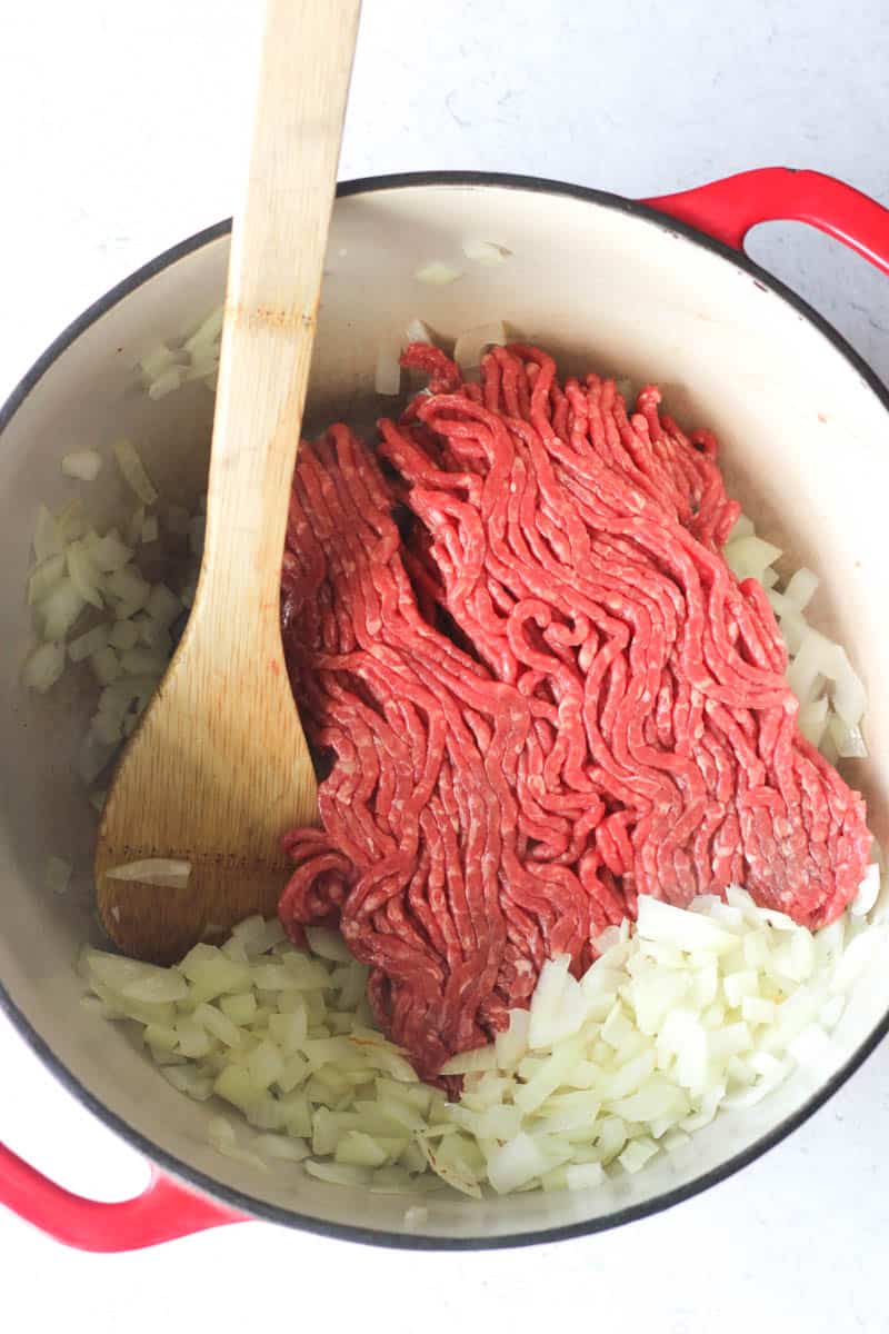 ground beef and chopped onions in a big red pot