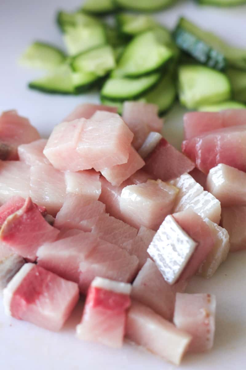 raw yellowtail cubed with sliced cucumbers on a cutting board