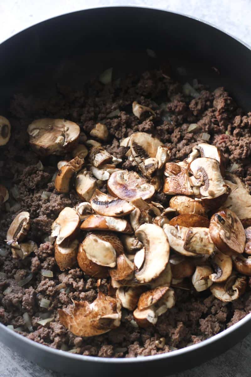 adding mushroom to ground meat in the skillet