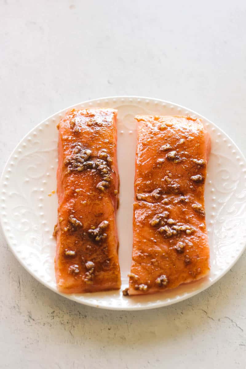 two raw seasoned salmon fillets on a white plate