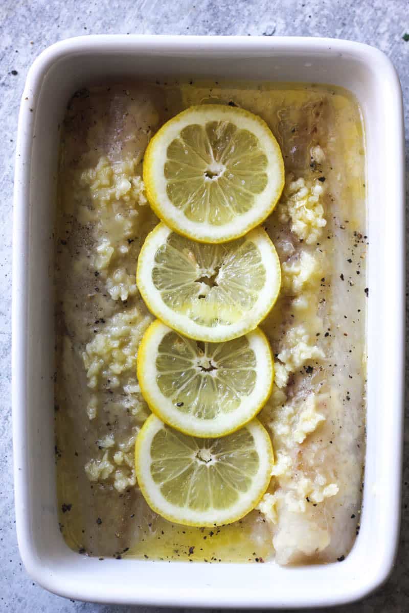 lemon slices on top of pollock fillets in the white baking dish