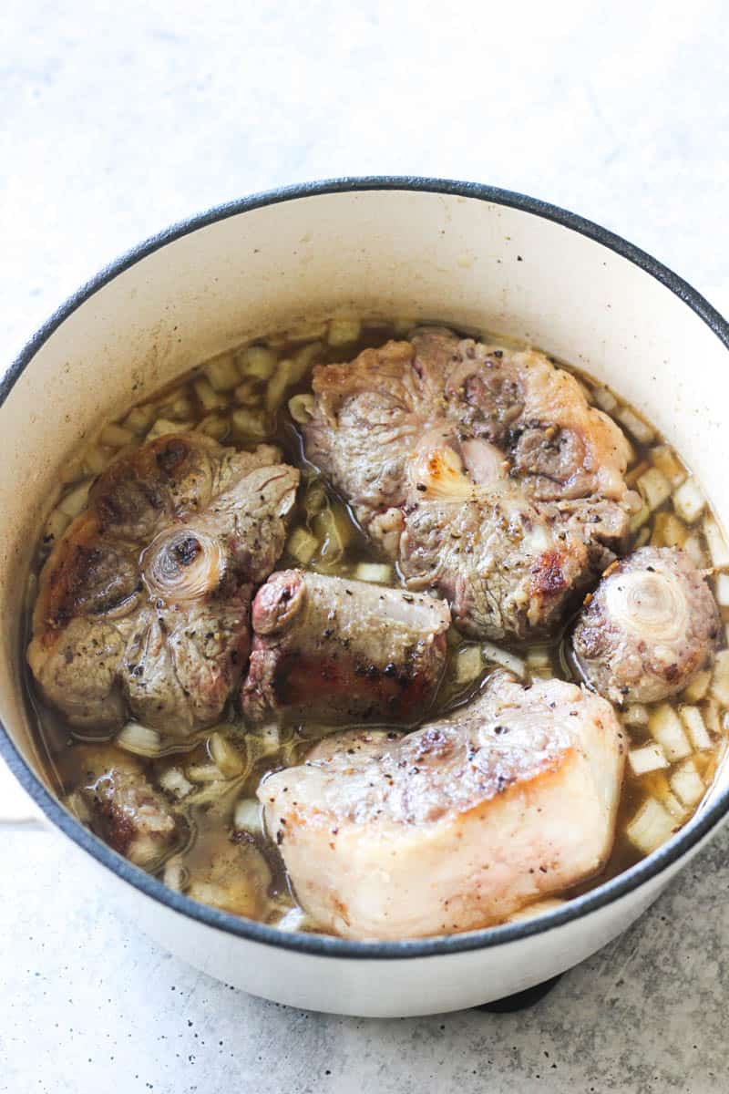 browning oxtails with onions in white pot