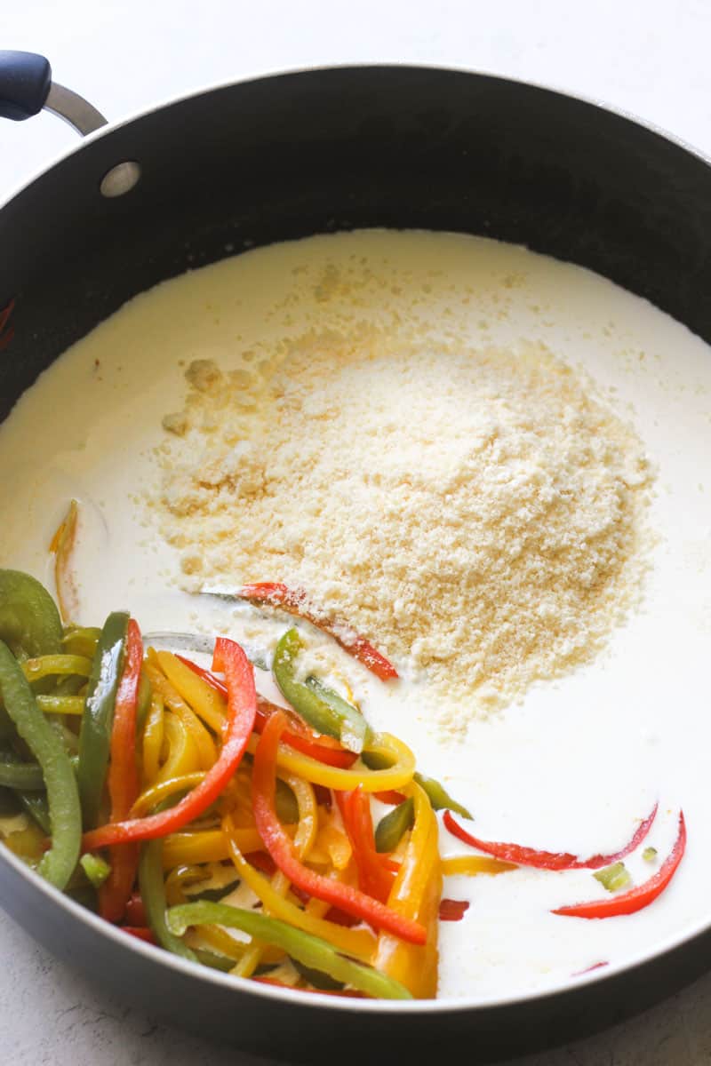 shredded Parmesan cheese on top of cream with bell peppers on the side in the large skillet
