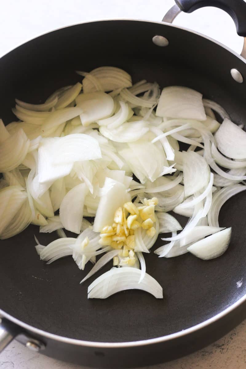 sliced onions with chopped garlic in a large black pan