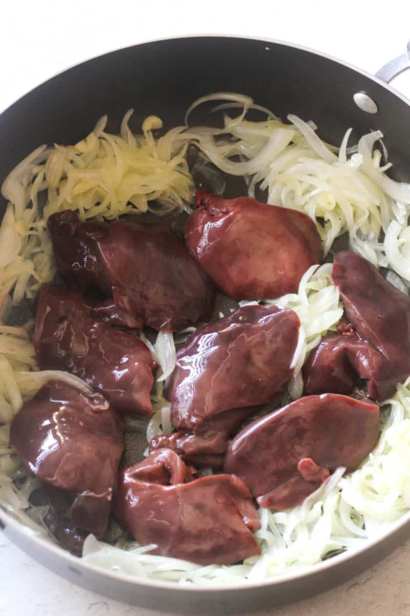 sliced onions sauteed with turkey livers in a large black pan