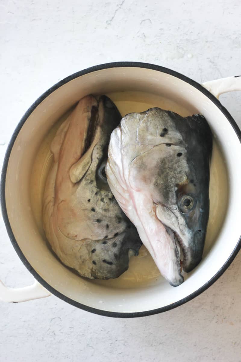 two raw salmon heads in the white heavy bottom pot