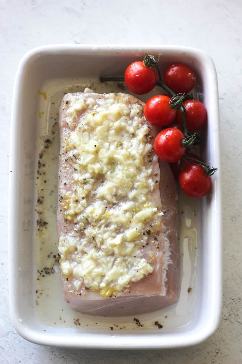preparing raw fish with garlic on top and cherry tomatoes on the side