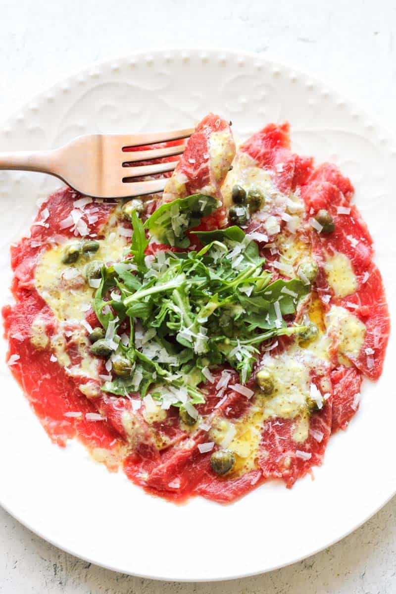 a piece of bison carpaccio on a fork on top of whole dish
