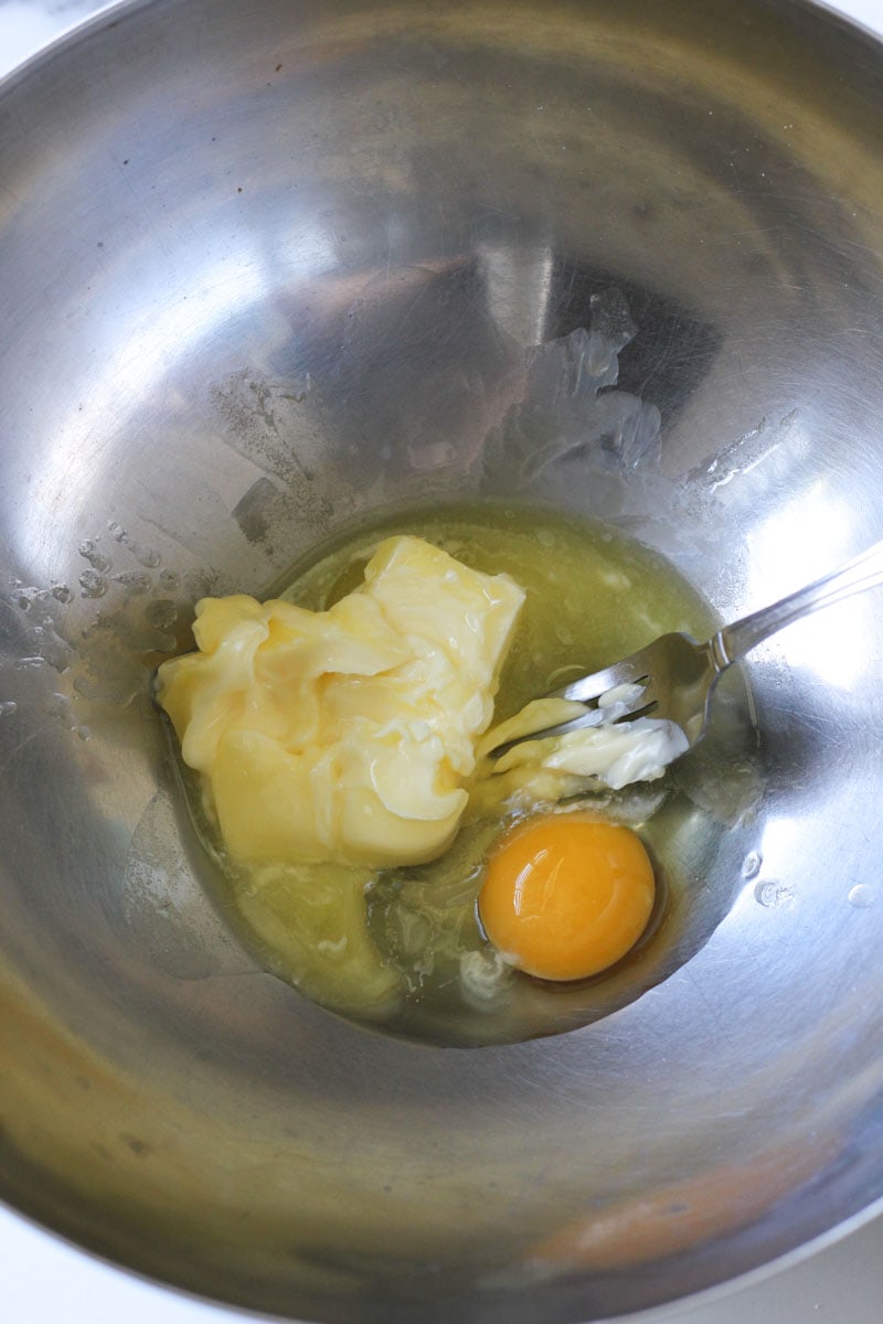 mixing soft butter with eggs in a large metal bowl