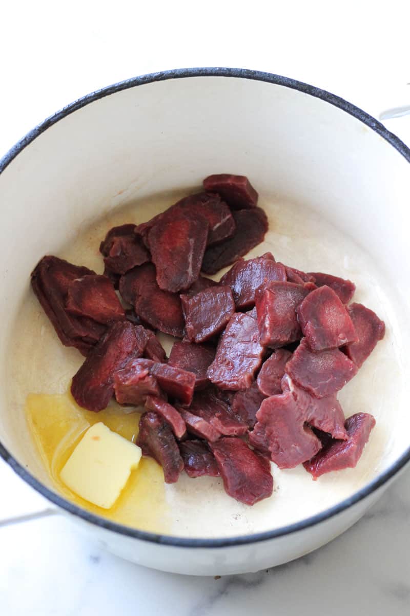 sliced red meat in the white pot with piece of butter