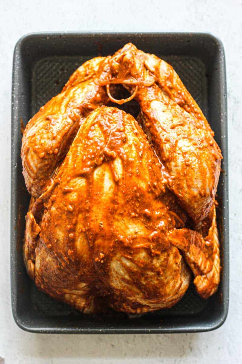 raw whole turkey covered in orange color marinade