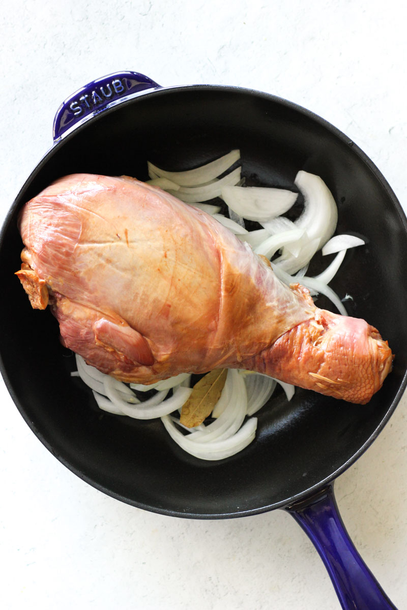 smoked turkey leg on top of onions in the blue pan