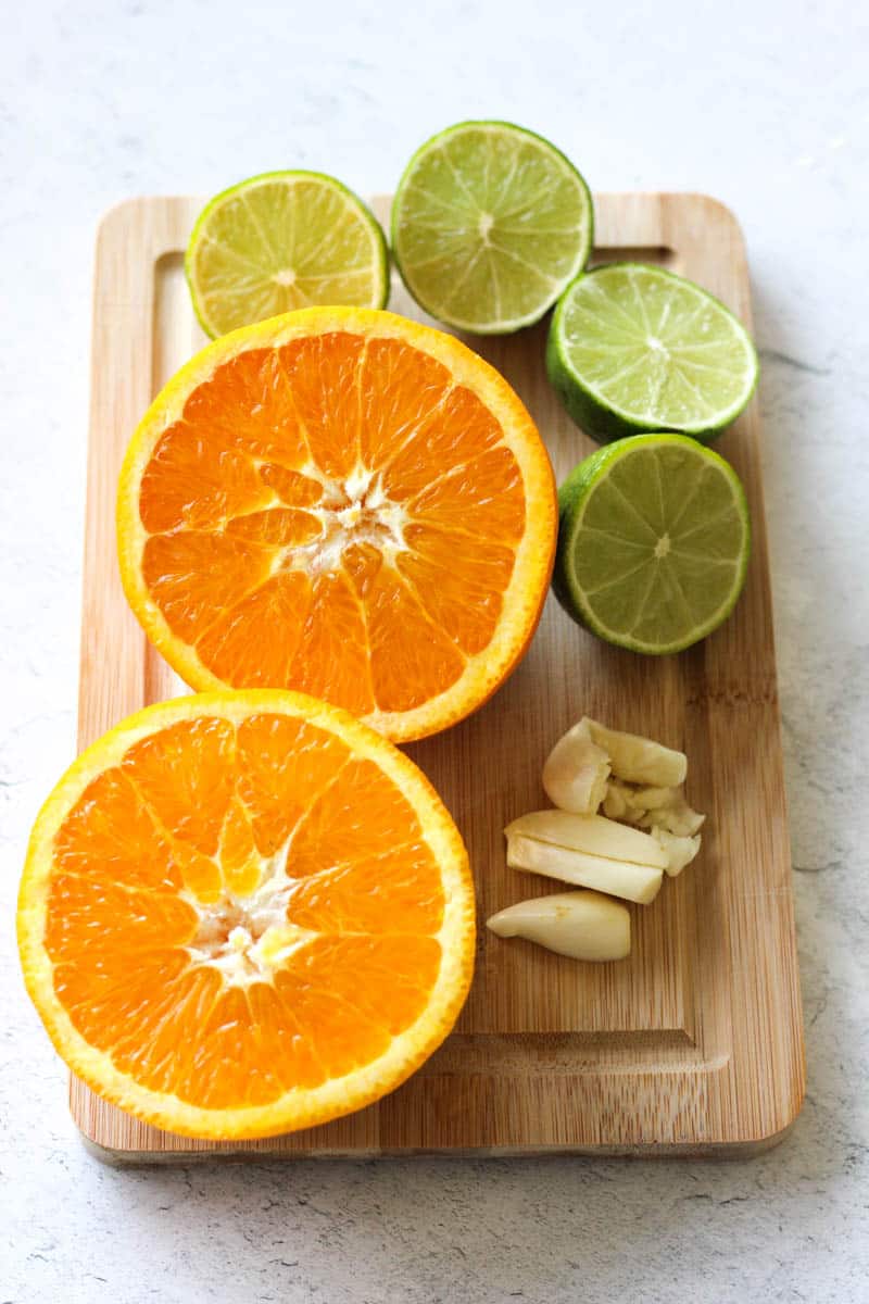 cut in half orange, lime and garlic on the cutting board
