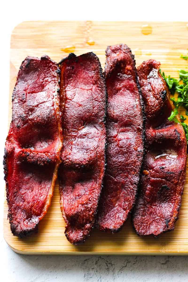 four pieces of duck bacon on the brown cutting board