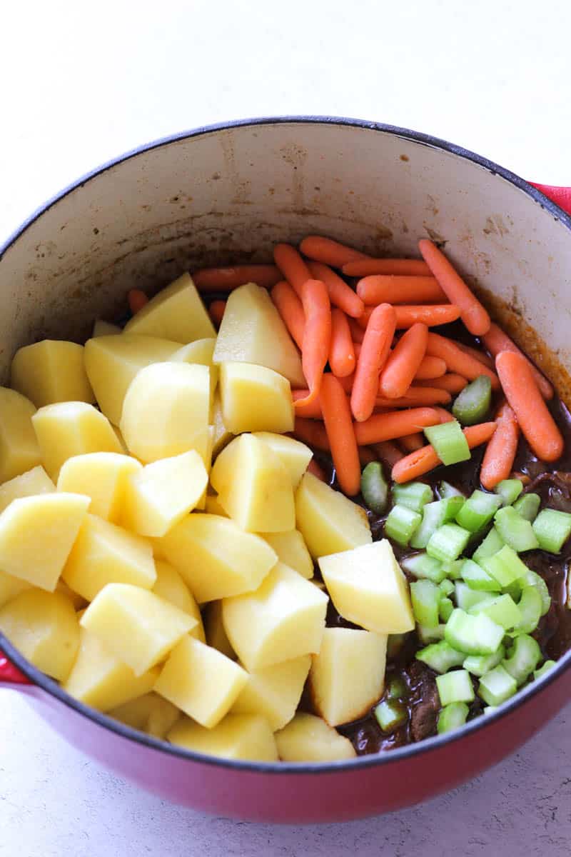 raw potatoes, carrots, celery on top of meat in a pot