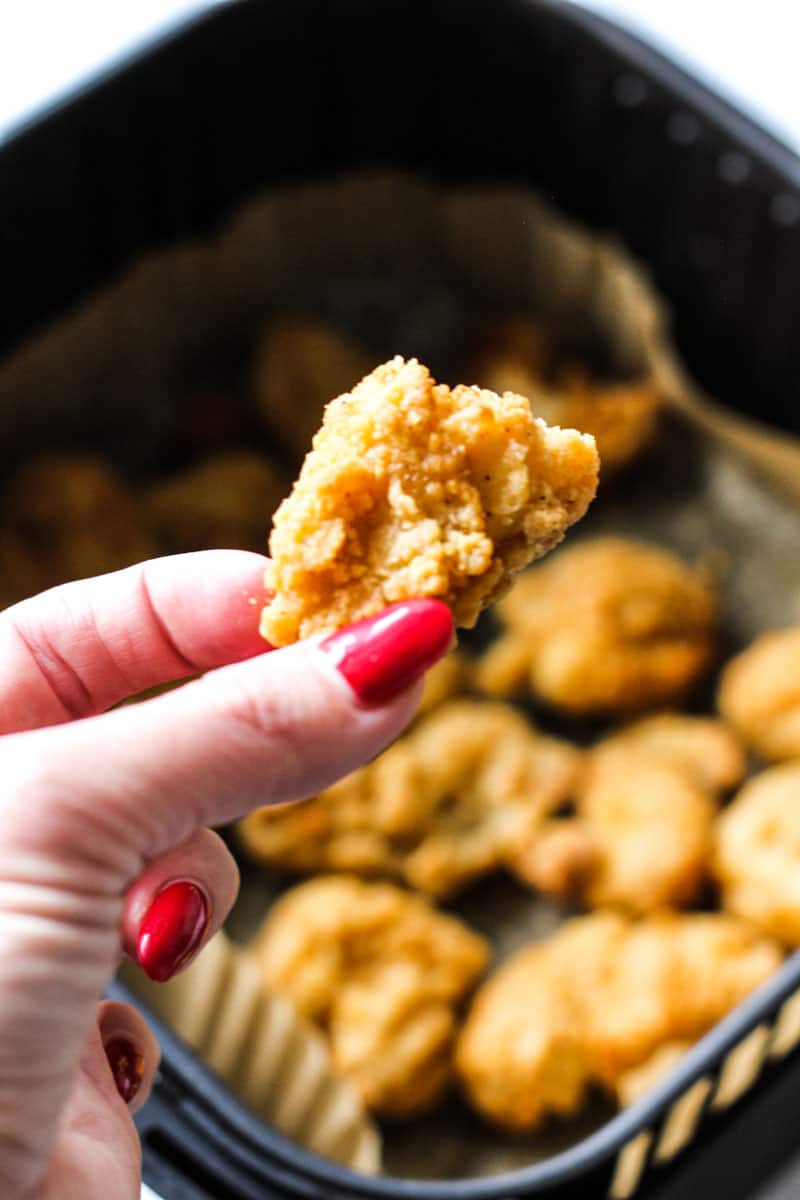 Any'tizers popcorn chicken in air fryer, holding one piece in hand