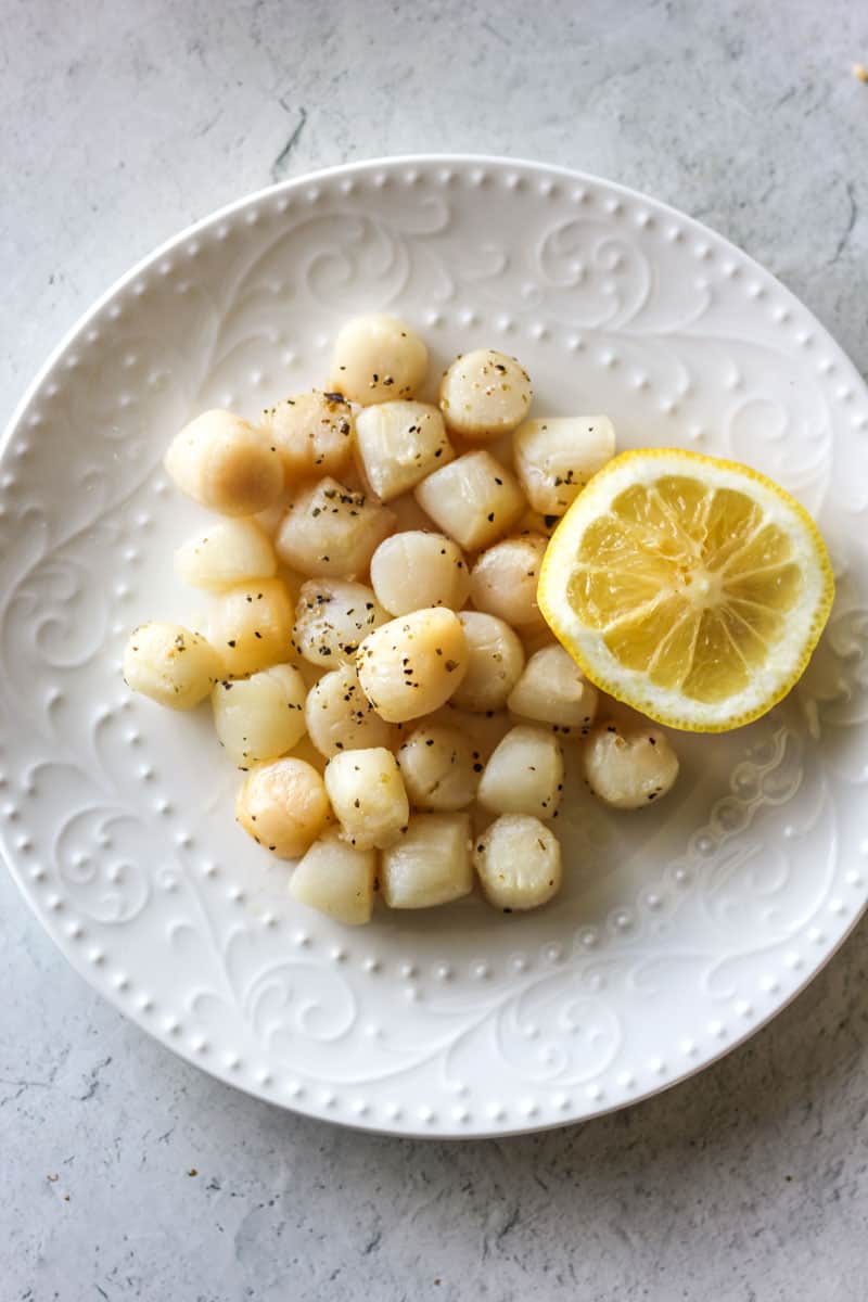 air fryer bay scallops on the white plate with half of lemon next to them