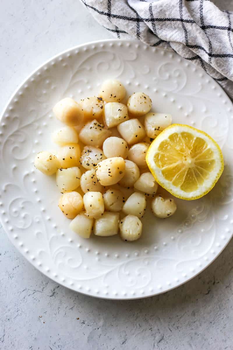 air fryer bay scallops on the white plate with half of lemon next to them