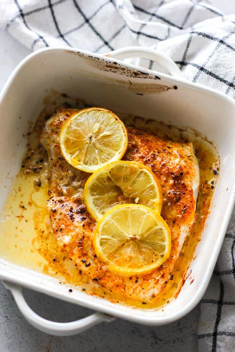 broiled baked walleye with lemon in a white baking dish