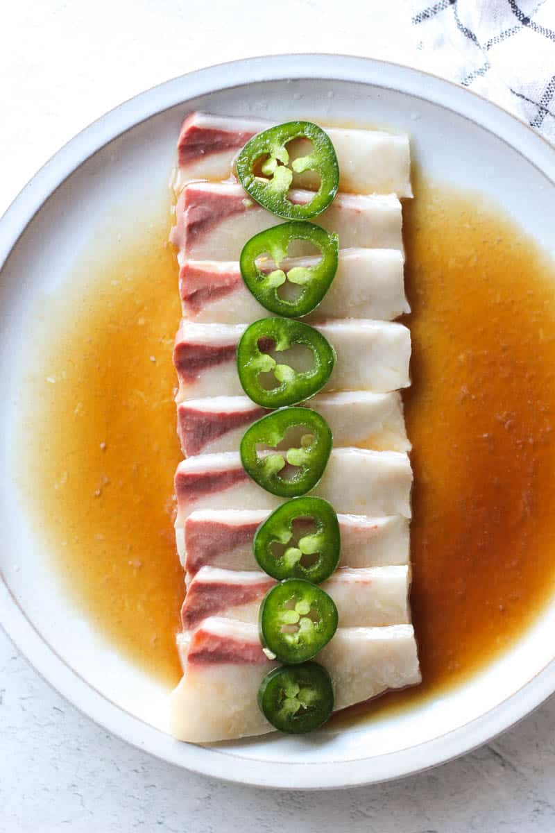 sliced hamachi carpaccio on the plate with jalapenos on top and covered in marinade