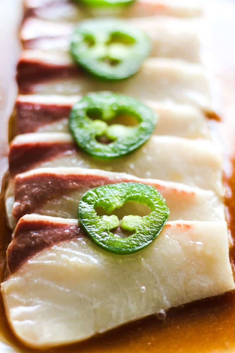 sliced hamachi carpaccio on the plate with jalapenos on top and covered in marinade
