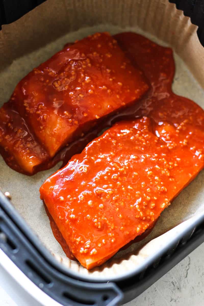 two salmon fillets in the air fryer covered in red sauce