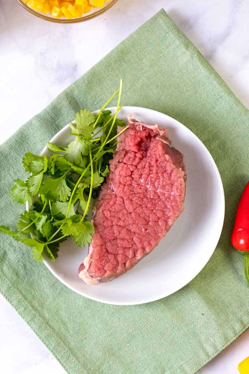 raw piece of meat on the plate with cilantro on the side