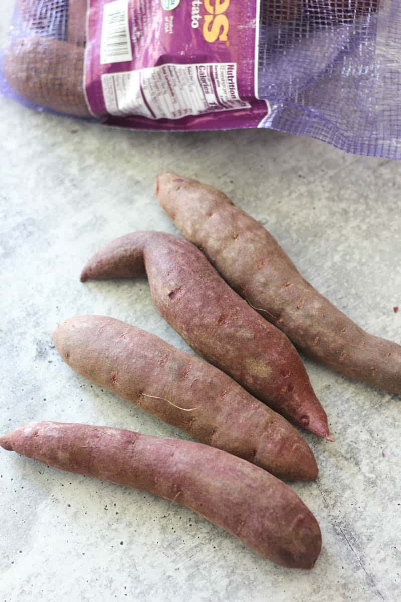 Fresh sweet potatoes on a light surface with a partially visible bag in the background.