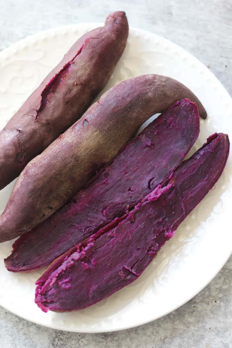 Fresh purple sweet potatoes on a white plate, ready to cook or serve.