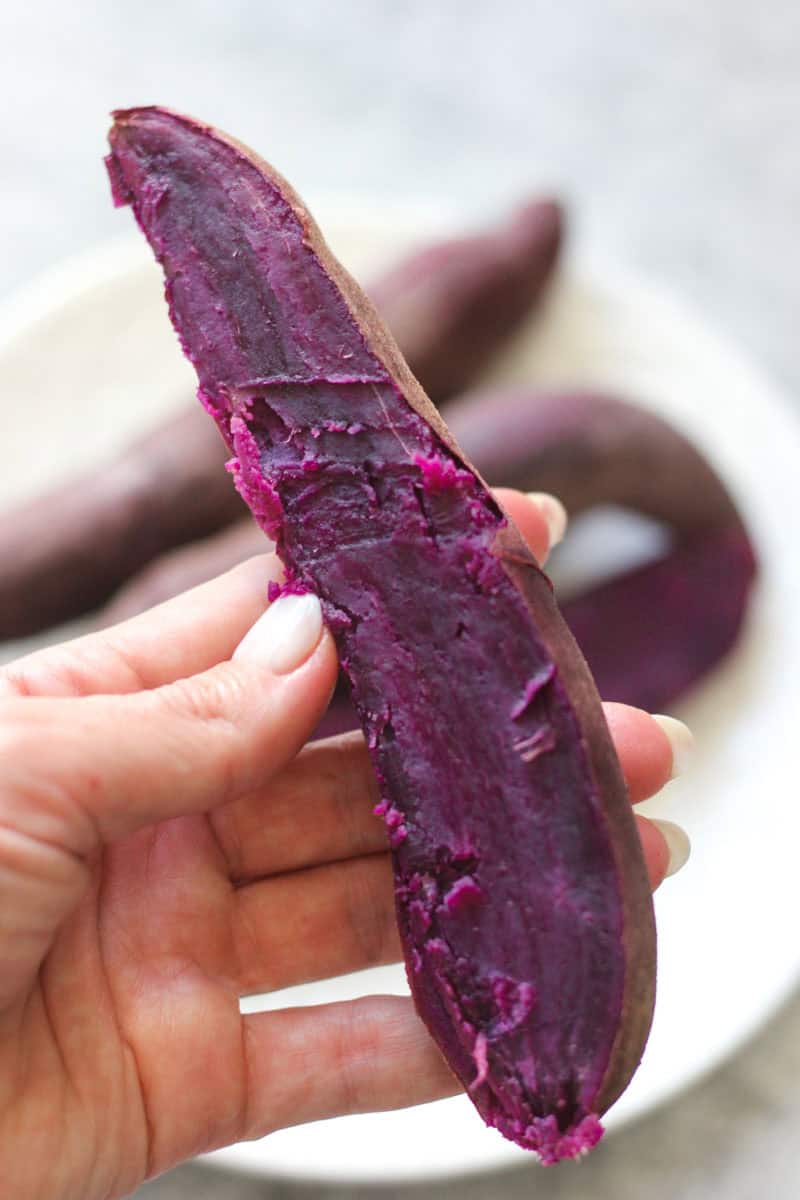 Fresh purple sweet potato held in hand, showcasing its vibrant color and texture.