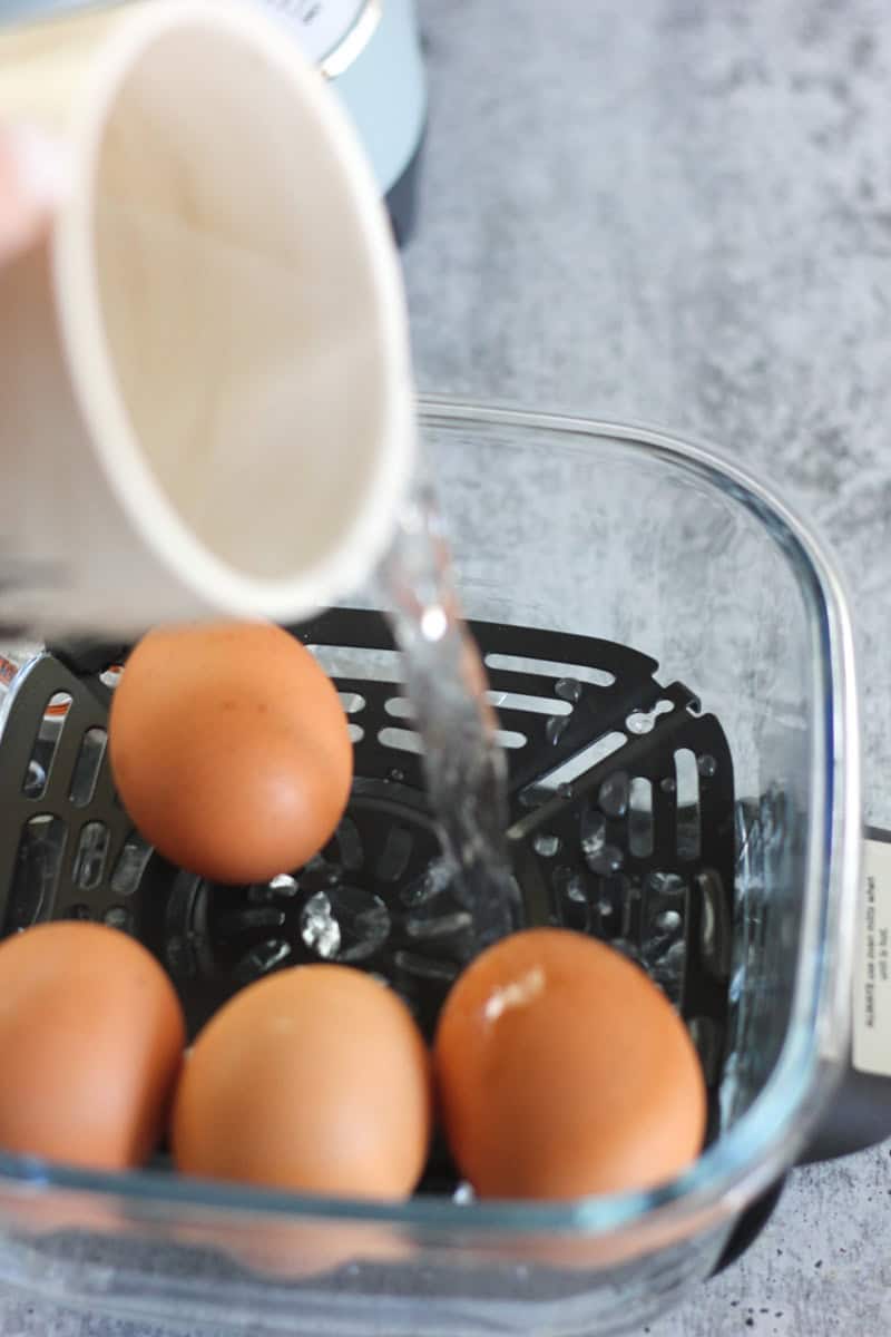 Eggs in a glass container with water being poured over them, suitable for cooking, baking, or breakf.