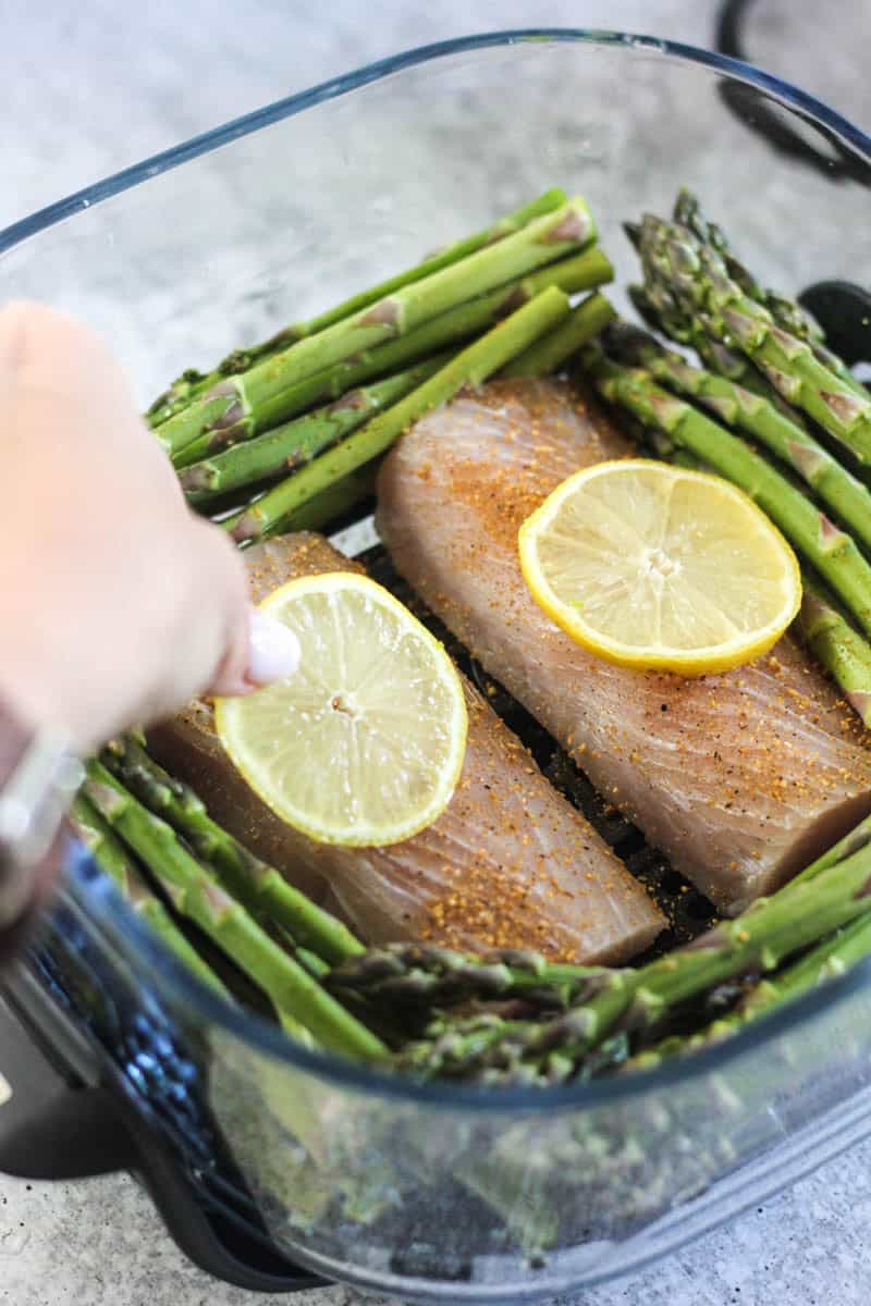 Baked salmon fillets with fresh asparagus and lemon slices in a glass dish.
