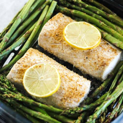 Baked fish fillets topped with lemon slices, served with fresh asparagus spears.