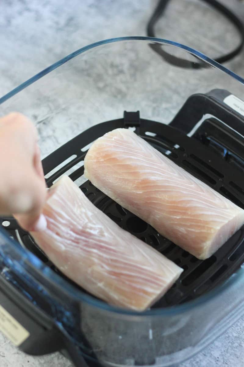 Air fryer chicken breasts ready for cooking, fresh and raw, in a black air fryer basket.