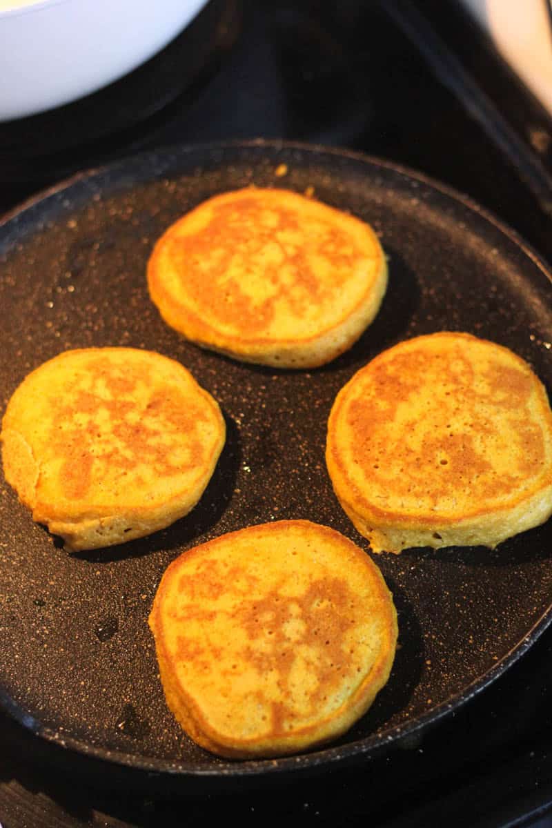 Five golden fried patties cooking on a black skillet.
