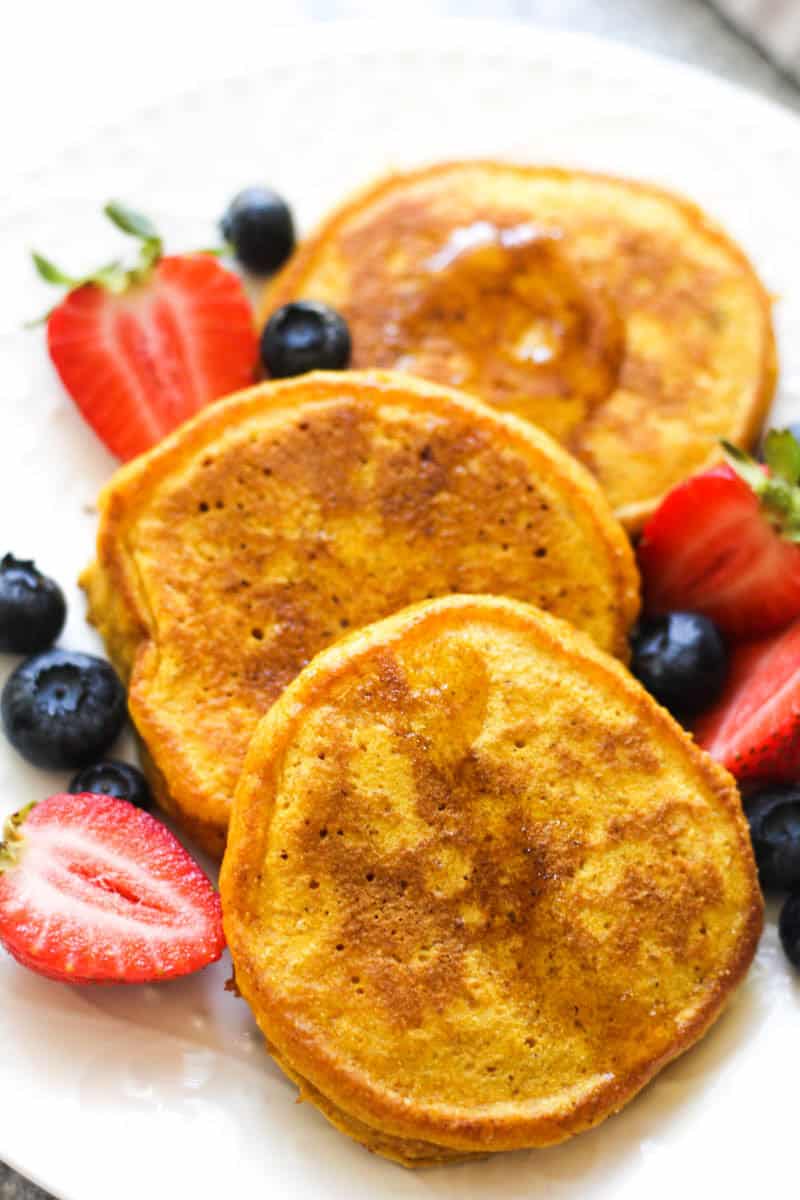 Golden French toast served with strawberries and blueberries on a white plate.