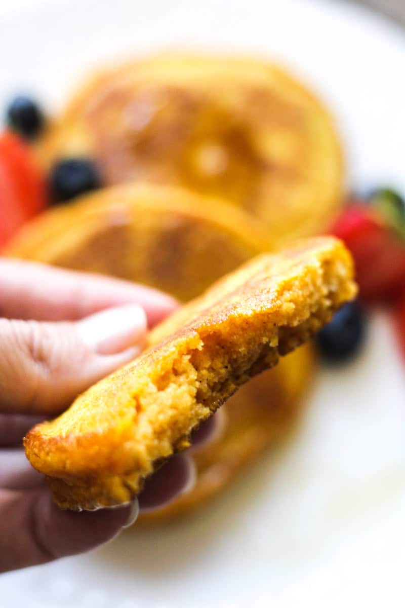 Close-up of a crispy cornbread slice with fresh berries in background.