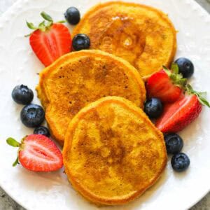 Golden French toast served with strawberries and blueberries on a white plate.