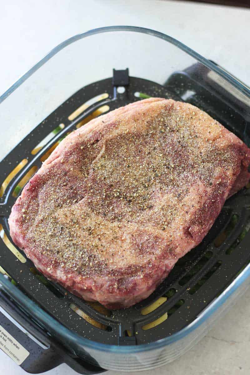 Raw beef roast seasoned with spices in a glass baking dish.