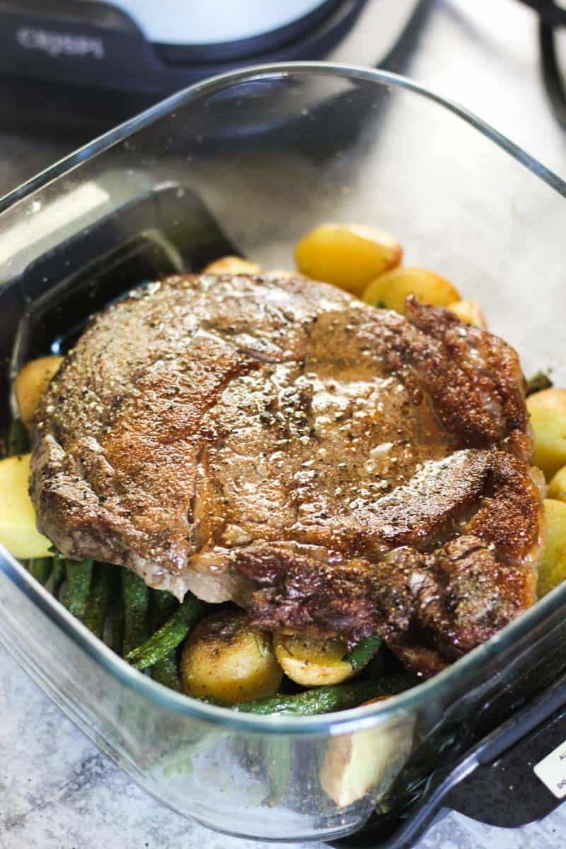 Roast pork with potatoes and green beans in a glass baking dish.