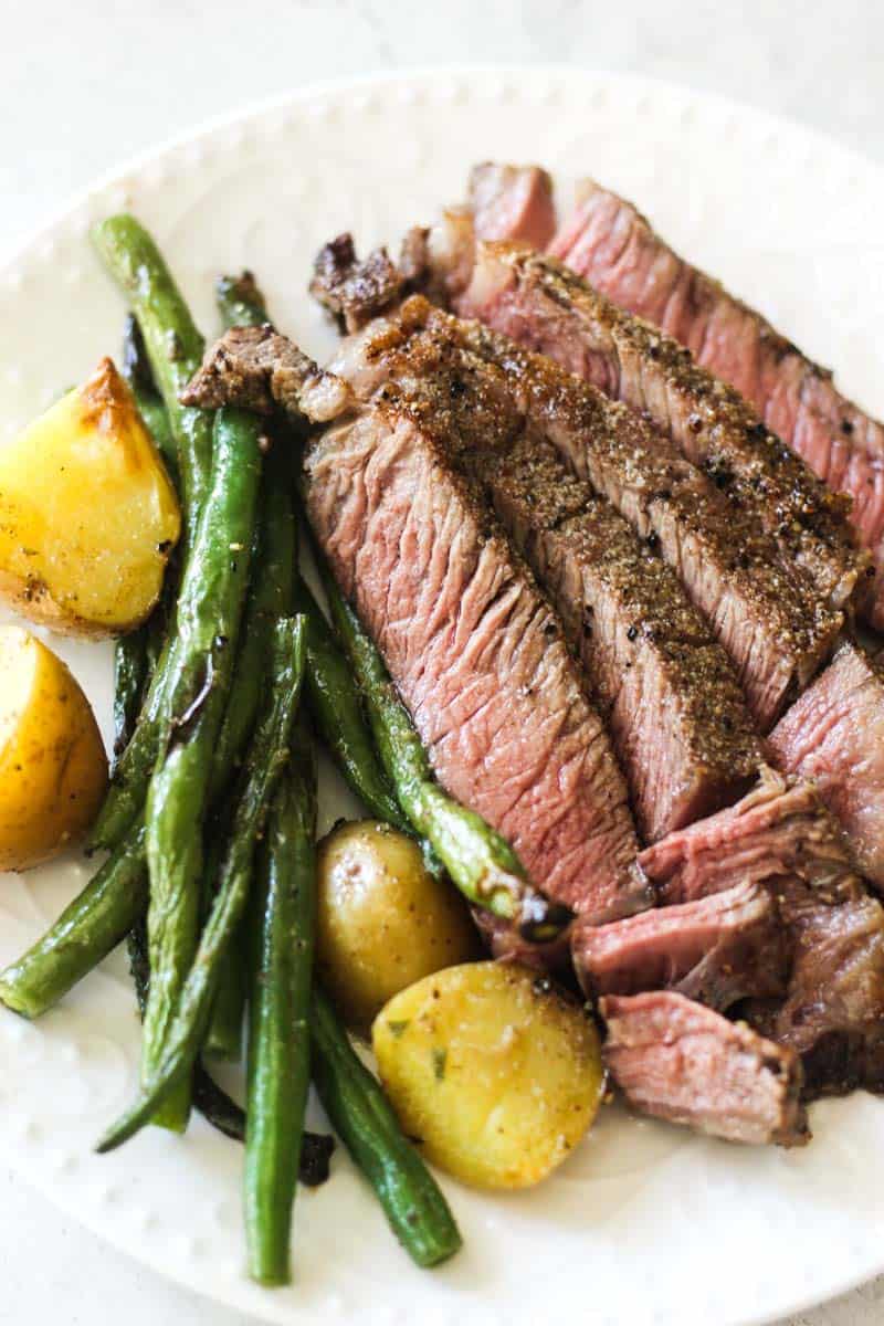 Juicy steak slices with green beans and roasted potatoes on a white plate.