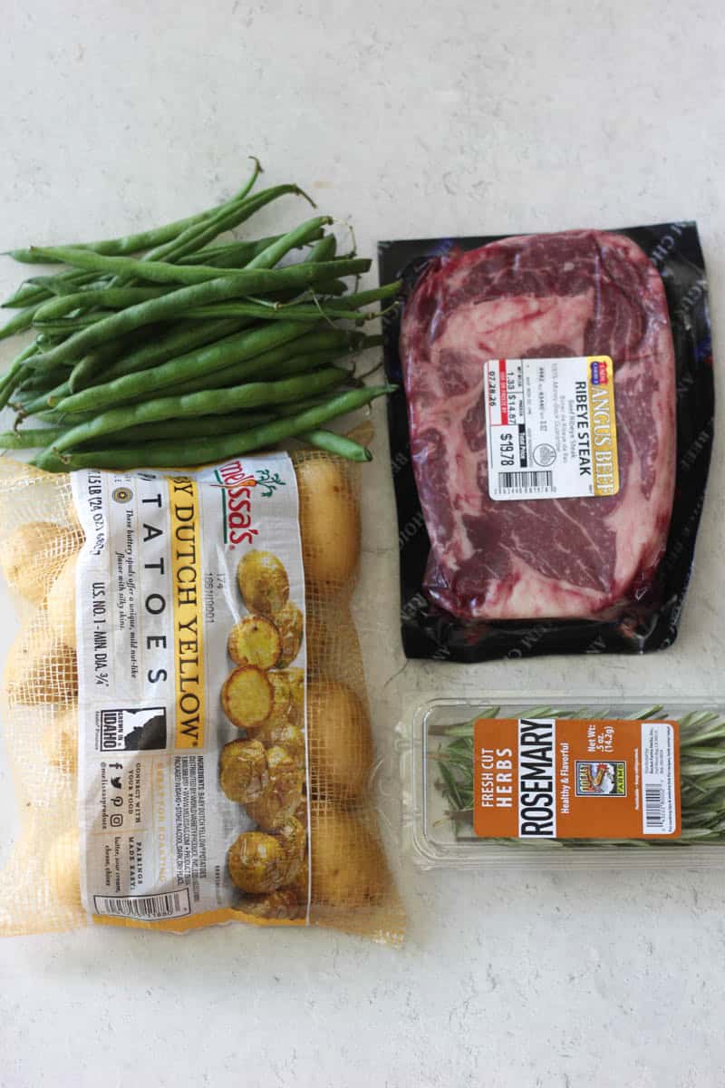 Fresh green beans, beef steak, yellow potatoes, and rosemary for meal preparation.