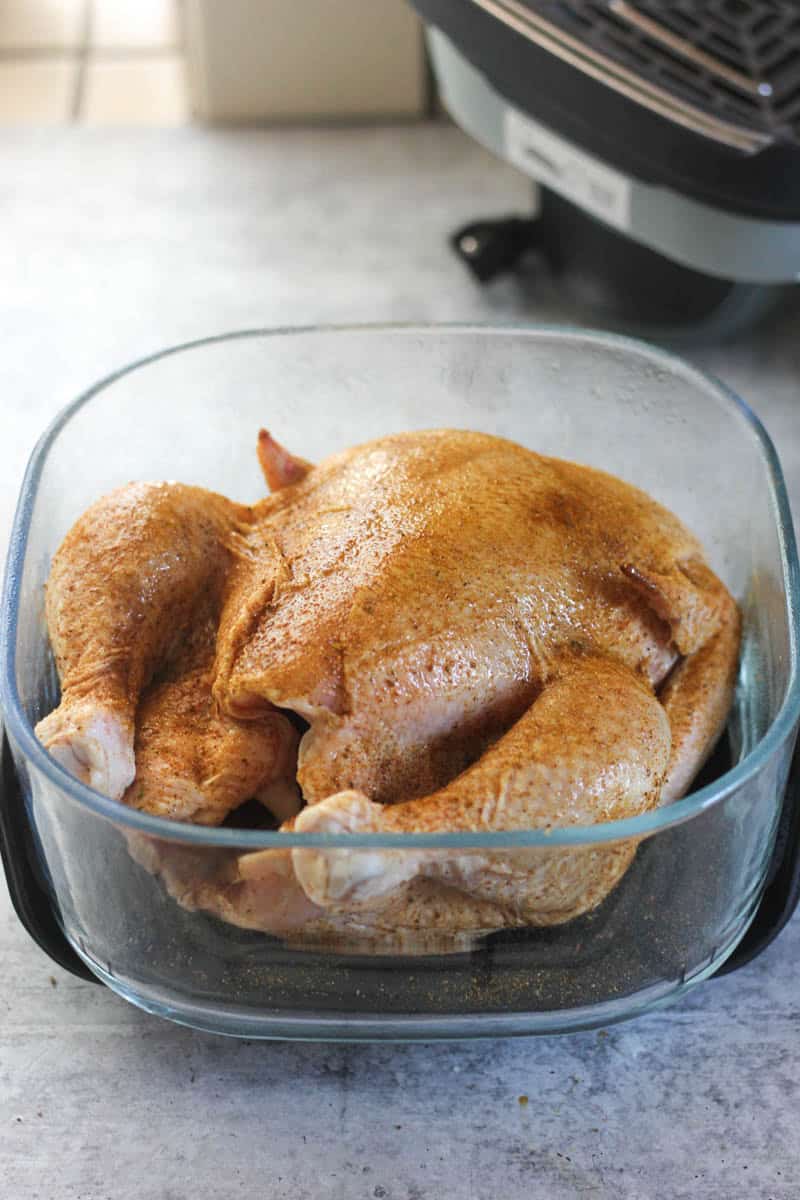 Raw whole chicken in a glass baking dish ready for cooking.