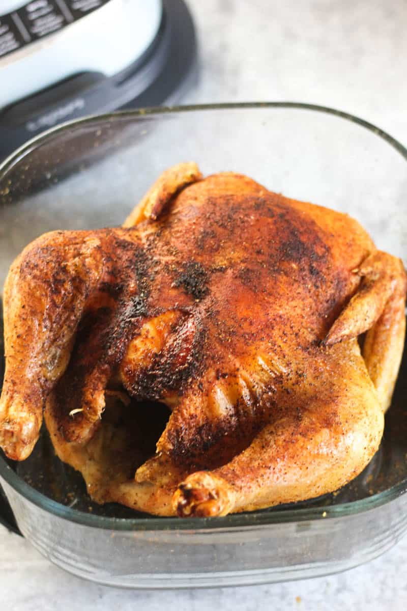 Juicy roasted whole chicken in a glass baking dish with crispy skin.