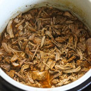 Tender shredded pulled pork cooking in a slow cooker with rich sauce.