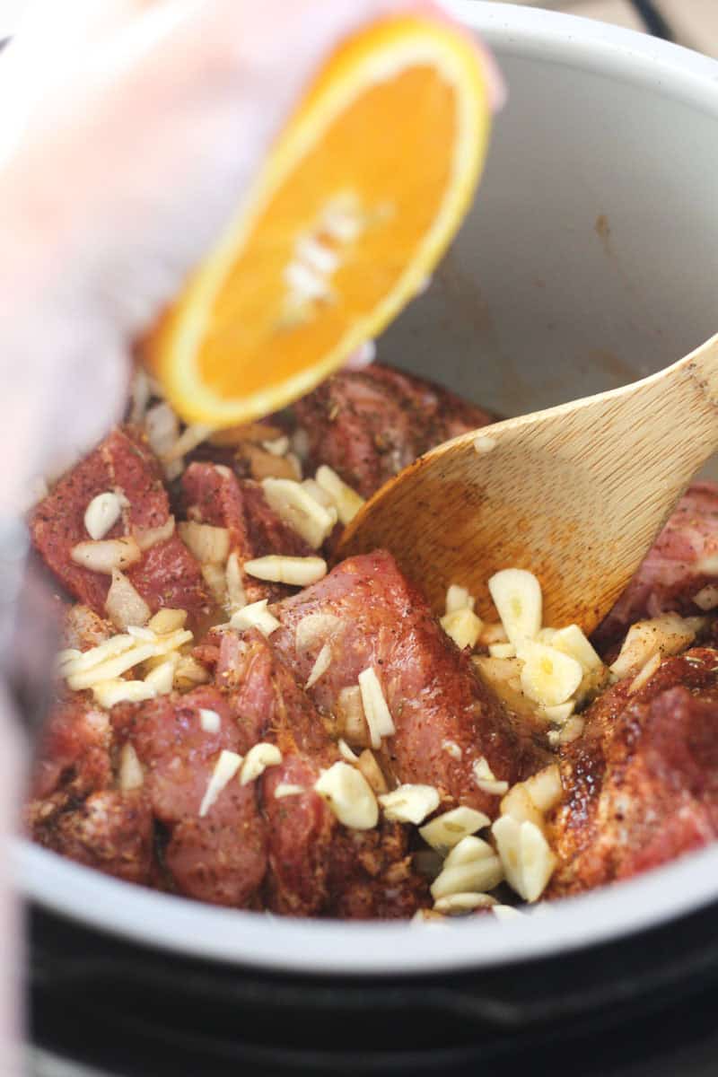 Beef stew with garlic and orange slice garnish in a pot.