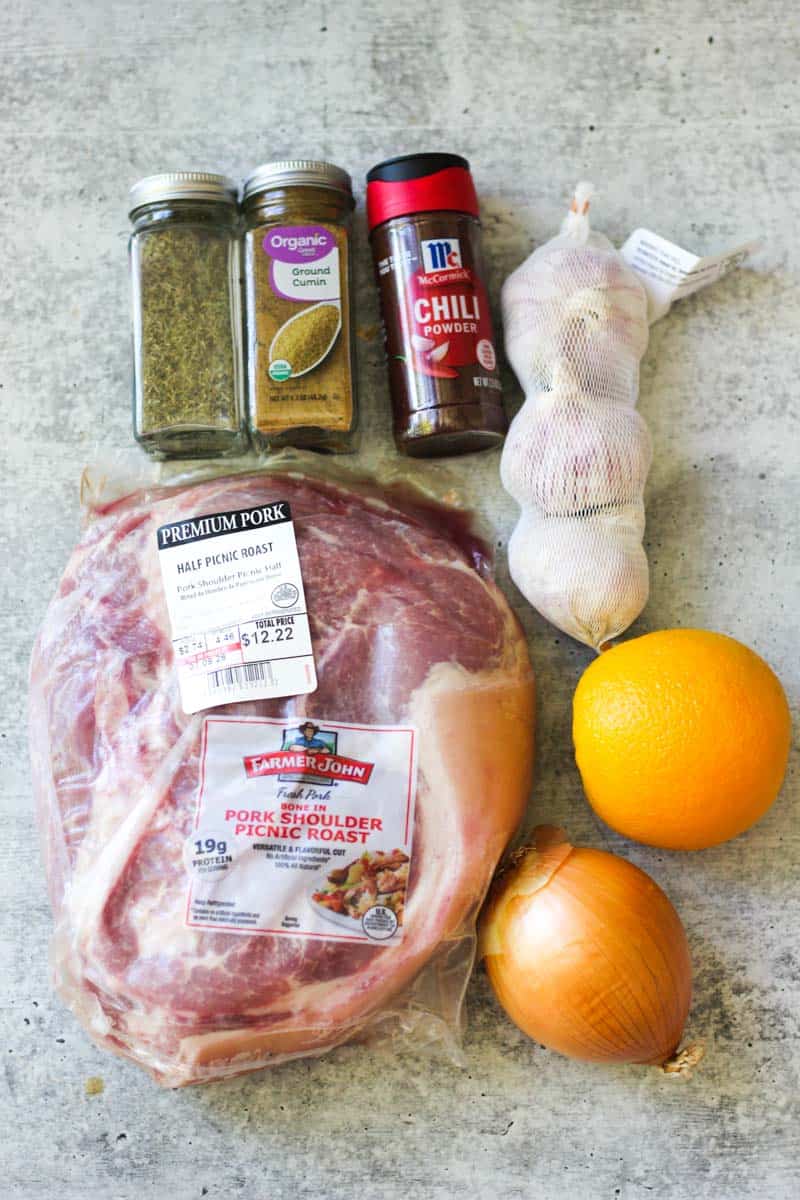 Fresh pork, garlic, onion, orange, spices, and chili powder for cooking.