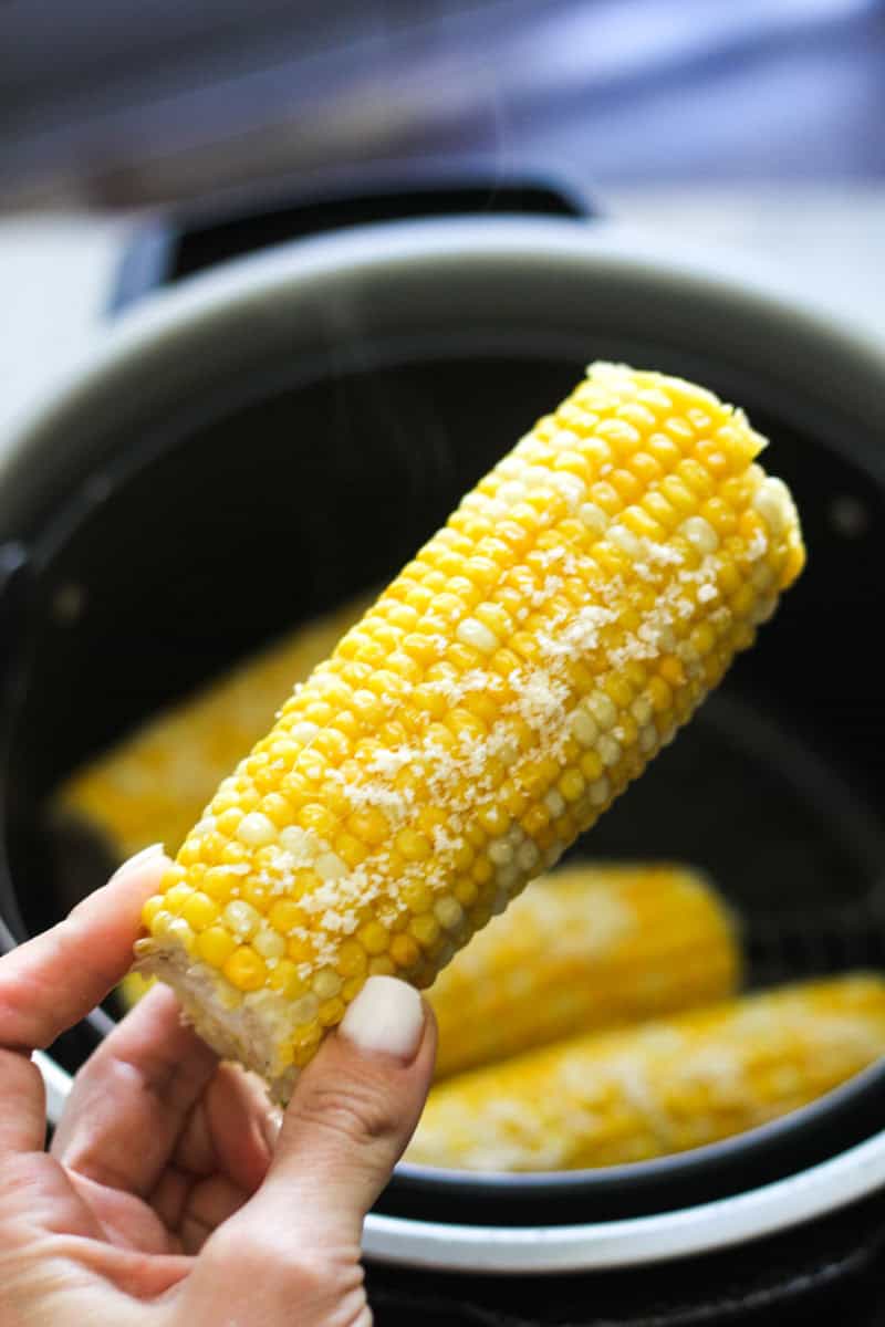 Close-up of a hand holding a cooked corn on the cob with butter.