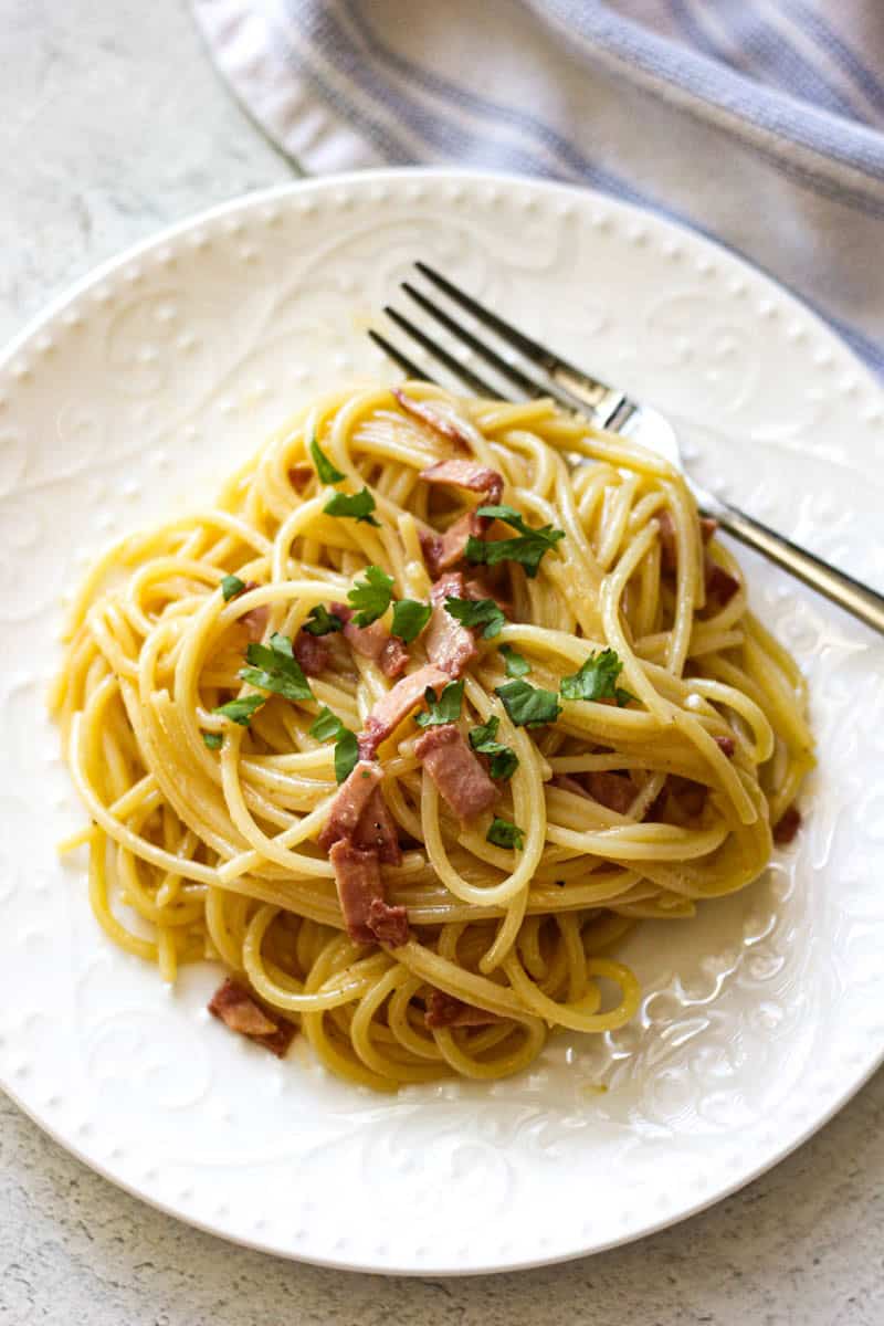 Delicious spaghetti carbonara with pancetta and parsley on a white plate.