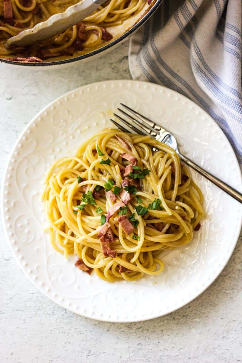 Delicious spaghetti carbonara with pancetta and parsley on a white plate.